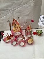 Photo showing the glass pitcher with gold leaf design and six matching glasses, each with plastic red or pink swizzle sticks.