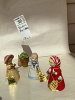 Front view of three bisque porcelain Merri-Bells figurines in pastel colors, each with seller tags showing 'Merri-Bells' branding.