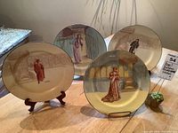Front view of four hand painted Royal Doulton Shakespeare character plates arranged on a table, showing detailed color illustrations of characters in historical costumes.