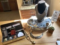 Photo of assortment of watches, costume rings, bracelets, necklaces arranged on a reflective tray and necklace stand with lot tag clearly visible.