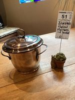 Silver plate thermal ice bucket on wooden table with tag showing lot info. Side handle and polished surface visible.