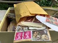 Box with a large envelope filled with various vintage cut-out stamps and loose stamps from different countries, some featuring postal markings and varying designs.