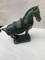 Front-side view of green carved stone horse sculpture showing details of saddle and reins.