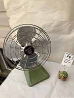 Photo of vintage Torcan metal table fan showing side angle with green base and metal cage with three blades