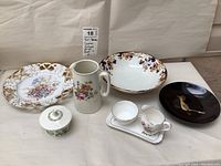 Seven pieces of serving and decorative ware; floral plates, jug, bowls, and cream and sugar set arranged on a white surface.