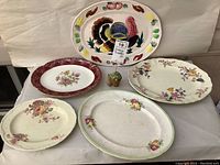 Five vintage platters displayed on a white surface including turkey design platter, floral pattern platters, and diverse sizes