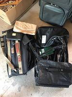 Photo showing the collection of bags including ROOTS wheeled duffle, Ascot garment bag, beige clutch, and wallets arranged on the floor.