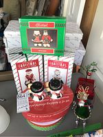 Overview of ceramic salt and pepper shakers shaped like snowmen, metal Christmas decorations (tree and reindeer), and boxed holiday plates.