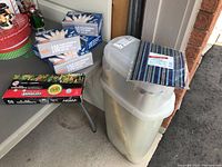 Five sets of Hobby Lobby 100 bulb indoor/outdoor super bright clear mini light sets in boxes, one set of Noma multicoloured indoor mini lights in box, and a Rubbermaid gift wrap storage container with materials inside.