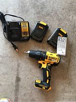 DeWalt cordless drill with charger and two batteries arranged on concrete floor.