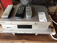 Panasonic VHS player and JVC DVD/CD player stacked with three remotes on top
