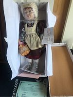 Full view of porcelain doll Nora in box with packaging, bubble wrap and certificate of authenticity included.