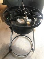 Front view of the coated metal propane burner with circular burner head, metal grate, hose and legs visible.