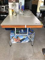 Front view of oversized table showing laminate top, wooden edge and metal legs, with items on the table and boxes underneath.