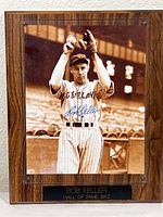 Full view of the autographed mounted photo showing Bob Feller in baseball uniform holding a ball overhead, displayed on a wood finish plaque.