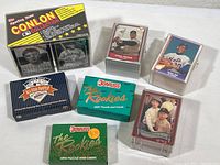 Overall view of seven boxed baseball card sets and loose card stacks