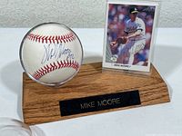 Autographed baseball in clear plastic case and Mike Moore baseball card displayed on wooden stand with nameplate