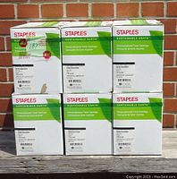 Six sealed boxes of Staples Sustainable Earth remanufactured toner cartridges stacked 3 on top and 3 below against a brick wall.