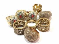 Nine gold tone Swarovski rings with wide bands and pave setting crystals in various styles including dome-shaped, lattice pattern, and floral crystal designs. Rings show varying degrees of wear and missing or broken crystals.