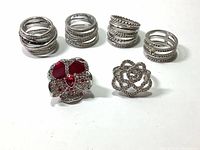 Front view of 7 rings including 5 layered silver tone rings with pave crystals and 2 floral design rings with red enamel and crystals
