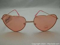 Photo showing a front view of a pair of heart shaped sunglasses with rose gold metallic frame and rose colored lenses with white accents, UV rated.