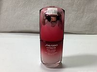 Front view of a 30ml sealed bottle of Shiseido Ultimune serum, showing gradient color from white to red with a price tag of $51.