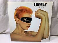 Front cover of Eurythmics Touch 1984 album showing woman with orange hair and black eye mask in flexed arm pose.