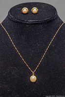 Necklace with pendant displayed alongside stud earrings on black stand