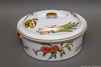 Front angle of the closed lidded oval casserole dish showing fruit decorations and gold trim.