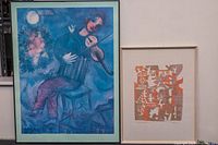 Photo showing both framed prints side by side: the blue-toned violin player print and the orange abstract print.