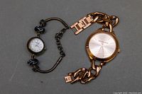 Two ladies watches including Caravelle by Bulova bracelet watch and Michael Kors watch laid side by side showing overall condition and style.