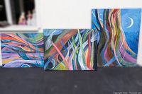 Three oil paintings displayed side-by-side against a wall, showing abstract flowing colorful brushstrokes with moon phases and nature themes.
