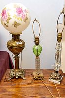 Three vintage lamps: large converted oil lamp with floral globe shade and two decorative glass-based table lamps, cords visible, untested condition