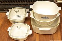 Set of five CorningWare casserole dishes stacked with three glass lids on top, showing classic blue cornflower and floral pattern designs.