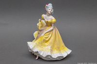 Full front angle of the Ninette Royal Doulton figurine showing details of yellow dress with white ruffles and floral designs.