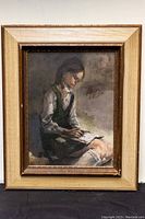 Full view of the framed oil painting showing a girl writing, held in a beige and gold wooden frame.