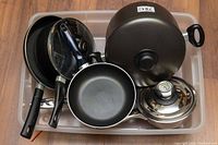 Top view of pots and pans in plastic bin showing frying pans, saucepans, and lids