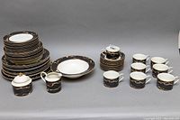 Full set of Mikasa Travertine Black chinaware spread showing plates, bowls, mugs, creamer, and sugar bowl with lid on grey background