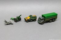 Four die-cast military toys including army truck, armored personnel carrier, artillery cannon, and fighter plane with camouflage paint.