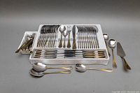 Entire flatware set arranged in molded plastic tray showing forks, spoons, knives, and serving pieces with gold swirl handle accents.