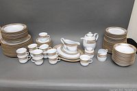 Full set including stacked plates, cups, saucers, and serving pieces arranged on gray background.
