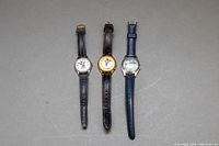 Three watches laid flat: two Mickey Mouse with black leather straps and one Wayne Gretzky watch with blue strap.