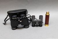 Full view of the lot showing three items: large black vintage 7x35 binoculars with leather case, small gray mini binoculars, and brass TASCO pocket spy glass