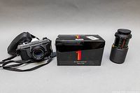 Camera in leather half-case with strap, boxed Vivitar lens and Makinon lens with caps on grey background