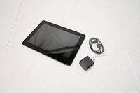 ASUS tablet with charger and USB cable on a white surface, screen visible with some smudges.