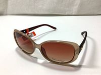 Side angle view of sunglasses showing beige plastic frames and brown arms with label tag still attached.