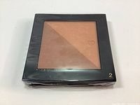 Top view of the bronzing powder duo showing dual triangular shades in sleek black compact case, labeled shade 2.