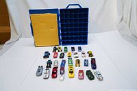 Open blue plastic Hot Wheels 48 car carry case showing yellow foam padding and blue grid compartments with 28 assorted die-cast cars in front.