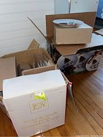 Multiple boxes shown including original packaging labeled 'Holiday Joy' and images of holiday-themed plates and cups with Christmas tree and snowman motifs.