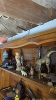 Wide view of wooden shelf with various figurines including birds, elephant, giraffe, coffee pot, and stein